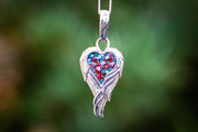 Photograph depicts the angel Wing Heart Pendant hanging from a chain. The pendant contains red and turquoise crushed opal. Necklace for ash, necklace for cremation ash, necklace for cremains, angel necklace